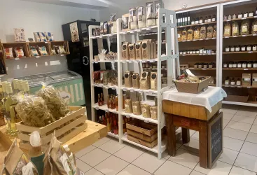 Ein kleiner Laden mit Regalen voller Lebensmittel und Produkten. Auf der Theke stehen frische Waren und verpackte Artikel zum Verkauf.