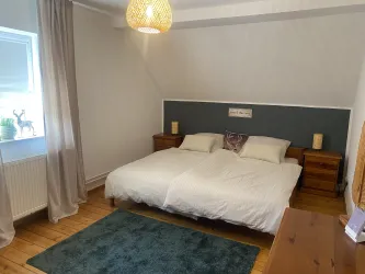 Ein gemütliches Schlafzimmer mit zwei Einzelbetten, Holzkommoden und einem großen Teppich. Die Wände sind hell gestrichen, und es gibt eine Deckenleuchte sowie Vorhänge.