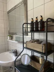 Ein modernes Badezimmer mit einem eleganten Spiegel und einem offenen Regal. Auf dem Regal stehen Pflegeprodukte und frische Handtücher.