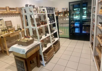 Ein einladendes Geschäft mit Regalen, die mit verschiedenen Lebensmitteln gefüllt sind. Auf der linken Seite befindet sich ein Tisch mit Produkten und ein Kühlschrank im Hintergrund.