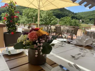 Ein schön gedeckter Tisch mit einem Blumenstrauß in der Mitte. Im Hintergrund sind grüne Hügel und Pflanzen zu sehen.