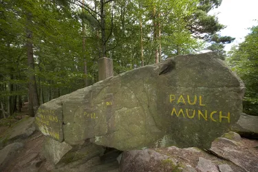 Ein großer, moosbedeckter Felsen im Wald mit der Aufschrift "PAUL MÜNCH". Umgeben von zahlreichen Bäumen und grünem Laub.