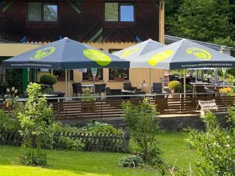 Unsere gemütliche Terrasse mit Sonnenschirmen und Tischen. Umgeben von einem grünen Garten mit Pflanzen.
