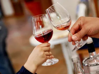 Zwei Gläser mit rotwein, die zum Anstoßen hochgehoben werden. Eine Hand eines Kindes und eine erwachsene Hand sind sichtbar.