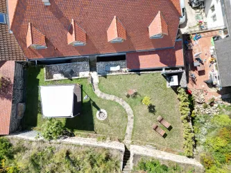 Eine Luftaufnahme des Gartens von unserem Mandelblütenhof. Der Garten verfügt über Rasenflächen, gemütliche Sitzmöglichkeiten in Sonne und Schatten und eine Feuerstelle.