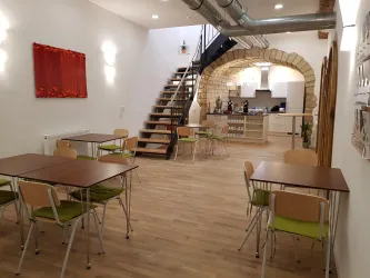 Das moderne Bistro mit einer steinernen Bogenarchitektur und Holzregalen. Ein gemütlicher Essbereich mit einem runden Tisch und frischen Blumen verleiht dem Raum eine einladende Atmosphäre.