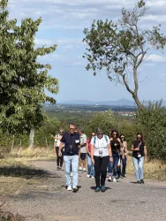 Eine Gruppe von Menschen wandert auf einem Weg durch die Natur. Im Hintergrund sind Bäume und sanfte Hügel zu sehen.