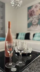 Eine stilvolle Wohnzimmereinrichtung mit einer Flasche Roséwein und zwei Gläsern auf einem Tisch. Im Hintergrund ist ein Kunstwerk mit einer Frau und Blumen zu sehen.