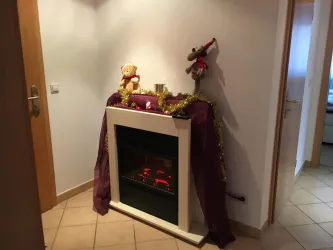 Ein dekorierter Kamin mit festlicher Beleuchtung steht in einem Flur. Auf dem Kamin befinden sich Weihnachtsfiguren und goldene Dekoration.