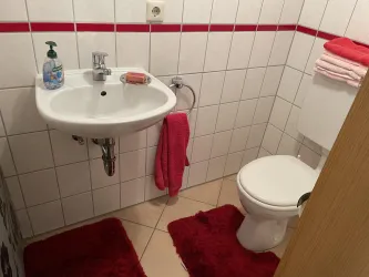 Ein kleines Badezimmer mit einem Waschbecken und einer Toilette. Rote Handtücher und Teppiche verleihen dem Raum einen frischen Akzent.