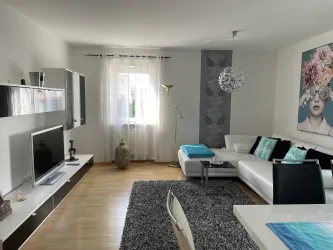 Ein modernes Wohnzimmer mit einem weißen Sofa und stilvollen Dekorationen. Der Raum ist hell und gemütlich, mit einem großen Fenster und einem Teppich.
