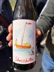 Eine Flasche Wein mit dem Etikett "Stresskiller". Das Etikett zeigt ein Boot auf dem Wasser mit einer bunten Illustration.