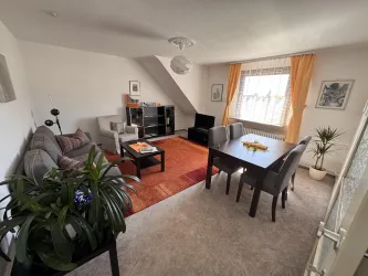 Wohnzimmer mit einer gemütlichen Sitzecke und einem großen Esstisch. Helle Fenster sorgen für viel Tageslicht und eine einladende Atmosphäre.