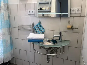 Ein modernes Badezimmer mit einem runden Waschbecken und einem großen Spiegel. Es gibt eine blaue Duschvorhang und Handtücher auf dem Waschbecken.