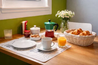 Ein Tisch mit einem Frühstücksarrangement. Es gibt eine Kaffeekanne, Croissants, Marmelade, Kekse und frischen Orangensaft.