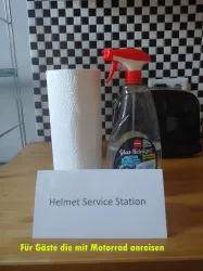Eine Helm-Service-Station mit einem Spray-Reiniger und Papiertüchern. Sie ist für Gäste gedacht, die mit dem Motorrad anreisen.