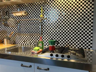 Eine moderne Küche mit einem schwarz-weißen Schachbrettmuster an der Wand. Auf der Arbeitsfläche stehen Geschirrspüler, Spülmittel und eine Kaffeemaschine.