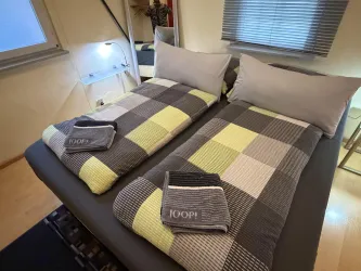 Ein gemütliches Schlafzimmer mit zwei Einzelbetten und bunten gestreiften Decken. Auf jedem Bett liegt ein Handtuch und es gibt eine angenehme Atmosphäre durch das natürliche Licht.