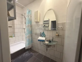 Ein modernes Badezimmer mit einer Dusche und Badewanne. Es hat helle Fliesen und einen stilvollen Spiegel.