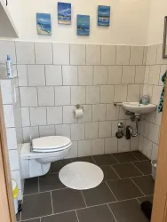 Ein kleines Badezimmer mit modernen Fliesen und einer Dusche. An der Wand hängen Bilder von Stränden und das WC ist ebenfalls vorhanden.