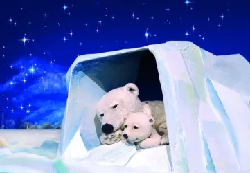 Ein Eisbärenpaar liegt gemütlich in einer Eis-Höhle. Der Nachthimmel ist voller funkelnder Sterne.