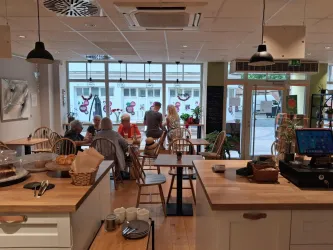 Ein einladendes Café mit holzernen Tischen und Stühlen. Gäste sitzen entspannt zusammen und genießen ihre Zeit.