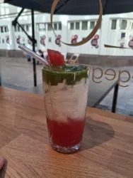 Ein erfrischendes Getränk in einem Glas mit roten und grünen Schichten. Oben mit einem Stück Wassermelone dekoriert und einem Strohhalm versehen.