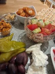 Ein kunstvoll angerichteter Teller mit verschiedenen Speisen. Darunter befinden sich Oliven, Salat, eingelegte Paprika und Dips.