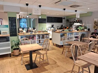Ein modernes Café mit Holzstühlen und Tischen. An der Wand steht eine Theke mit verschiedenen Snacks und Getränken.