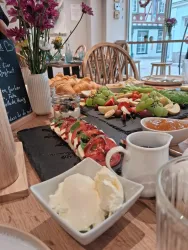 Ein schön gedeckter Tisch mit frischen Croissants, einer bunten Obstplatte und einer Caprese-Spezialität. Auf der Seite befinden sich Eiscreme und eine kleine Sauce.