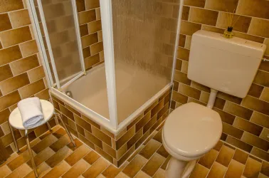 Ein modernes Badezimmer mit einer Dusche und einer Toilette. Die Wände sind mit braunen Fliesen bedeckt, und ein Handtuch liegt auf einem kleinen Tisch.