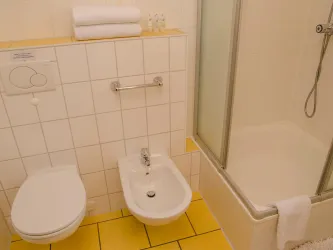 Ein Badezimmer mit einem Bidet, einer Toilette und einer Dusche. Die Wände sind hell gefliest und der Boden hat gelbe Fliesen.