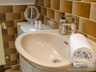 Ein modernes Badezimmer mit einem runden Waschbecken und einem Handtuch. Die Wände sind mit braunen Fliesen verkleidet und es gibt einen Spiegel sowie Pflegeprodukte auf dem Waschbecken.