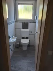 Ein modernes Badezimmer mit einer Toilette und einem kleinen Waschbecken. Die Wände sind gefliest und es gibt ein Fenster, das Licht hereinlässt.