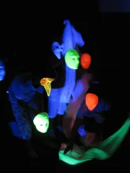 Eine Gruppe von leuchtenden Masken und Stoffen in einem dunklen Raum. Die Farben sind leuchtend und erzeugen eine geheimnisvolle Atmosphäre.