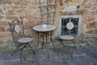 Ein kleiner Tisch mit zwei dekorativen Stühlen steht an einer steinernen Wand. Auf dem Tisch befindet sich ein kleiner Blumentopf.