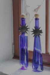 Zwei flaschenförmige Glasbehälter in tiefblau stehen auf einer Fensterbank. Sie haben eine Holz- und eine schwarze Sonnenfigur als Dekoration.