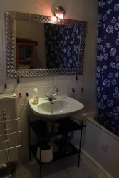 Ein Badezimmer mit einem Waschbecken und einem großen Spiegel. Die Vorhangstoffe haben ein maritimes Motiv in Blau und Weiß.