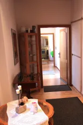 Ein heller Flur mit Holzfußboden und Teppichen. Auf der linken Seite steht ein Regal mit dekorativen Gegenständen.