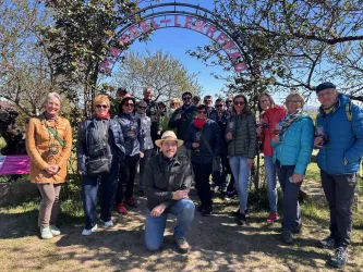 Eine Gruppe von Menschen steht unter einem bunten Tor. Es ist ein sonniger Tag mit klarem Himmel und einem schönen Naturhintergrund.