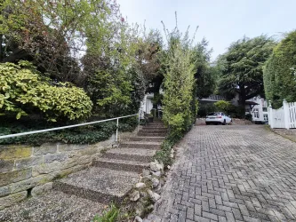 Ein geschmackvoll gestalteter Außenbereich mit einer Treppe und vielen Pflanzen. Im Hintergrund steht ein Auto auf einer gepflasterten Auffahrt.