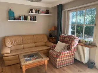 Das geräumige Wohnzimmer ist mit dekorativen Elementen gemütlich eingerichtet und bietet zur Terrasse hin Blick ins Grüne.