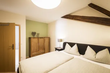 Ein gemütliches Schlafzimmer mit zwei Betten und einem Holzschrank. Die Wände sind in sanften Farben gehalten und es gibt rustikale Holzbalken.