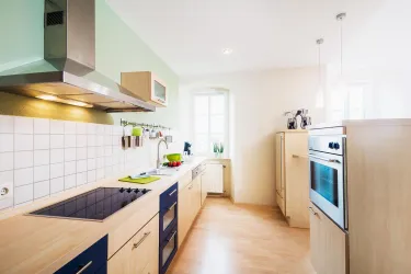 Eine moderne Küche mit Holz- und blauen Elementen. Sie hat große Fenster und ist hell erleuchtet.