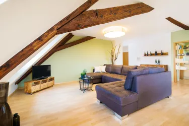 Eine moderne Wohnlandschaft mit einem großen Sofa und einem hellen Holzboden. Die Holzbalken an der Decke und die grünen Wände sorgen für eine gemütliche Atmosphäre.