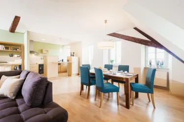 Ein modernes Wohn- und Esszimmer mit einem gemütlichen Sofa und einem Holztisch. Die blauen Stühle und das helle Licht schaffen eine einladende Atmosphäre.