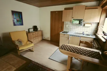 Eine gemütliche Küche mit einem Essbereich und einem Sessel. Die Holzdetails und das helle Licht sorgen für eine einladende Atmosphäre.