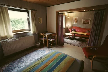 Ein gemütliches Zimmer mit einem Bett und einem Essbereich. Im Hintergrund befindet sich ein Wohnzimmer mit einer roten Couch.