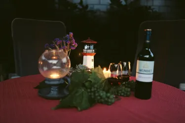 Ein schön gedeckter Tisch mit Rotwein, Kerzen und frischen Trauben. Ein kleiner Leuchtturm und Blumen verleihen der Atmosphäre einen besonderen Charme.