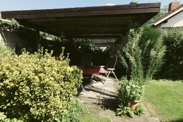 Ein einladender Gartensitzbereich mit einem überdachten Pavillon. Umgeben von grünen Pflanzen und einem gepflegten Rasen.
